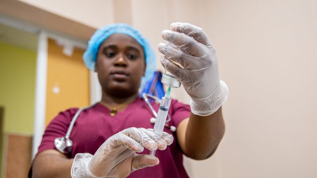 A nurse holds up a shot with gloves.