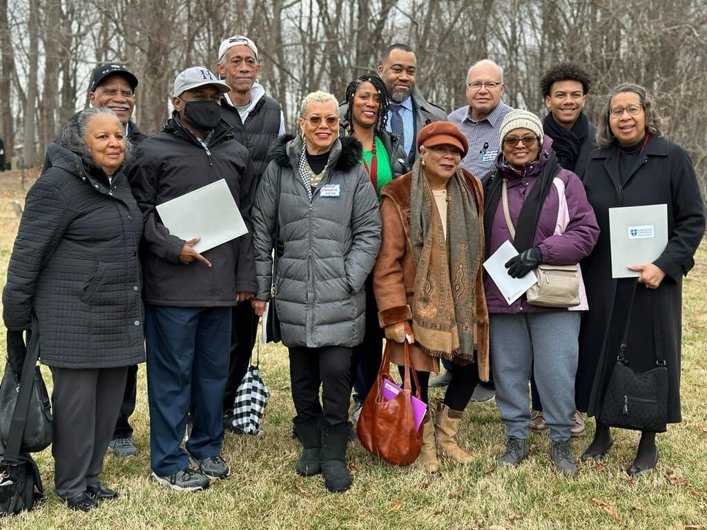 A group of men and women stand in winter jackets outside.