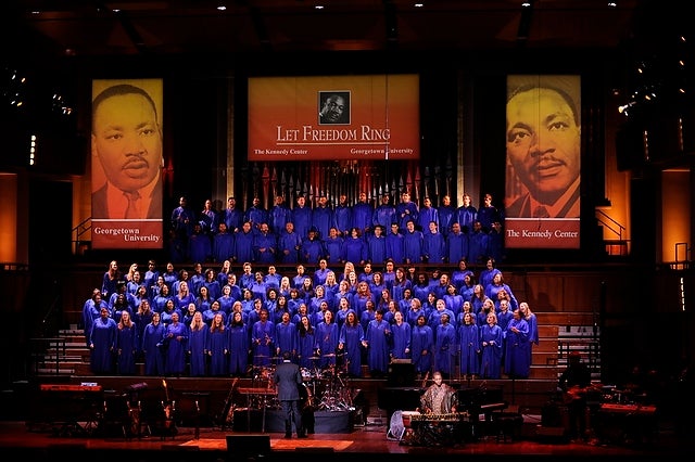 A choir dressed in blue robes perform on a stage at the Kennedy Center. On either side of them hang banners of Dr. Martin Luther King Jr.