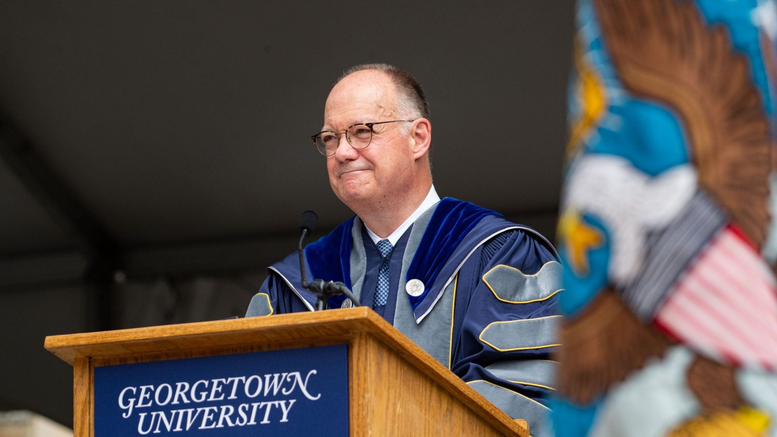 President John DeGioia looks out from a podium that says Georgetown University. He wears academic dress robes.