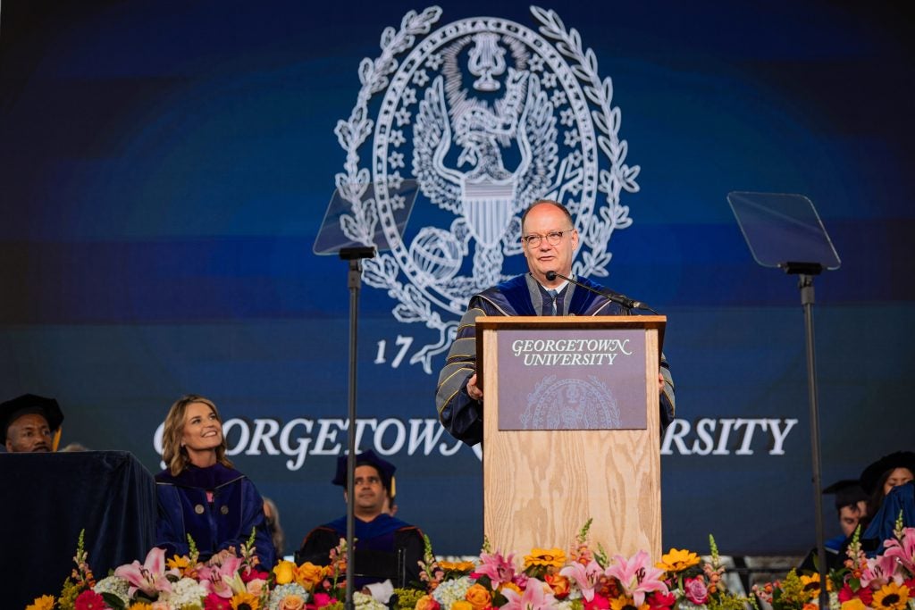 President DeGioia speaks in front of a podium with the Georgetown seal behind him on a stage.