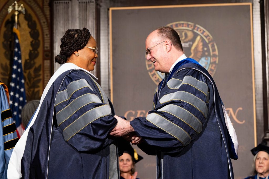 President DeGioia, dressed in a blue and gray academic robe, greets a Liberian peace leader in a blue and gray academic robe.