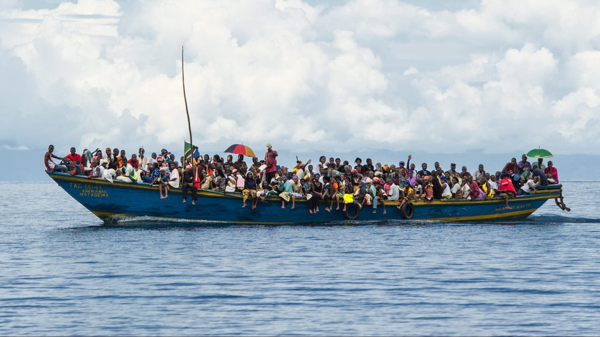 Small boat in a body of water with a crowd of people standing on it