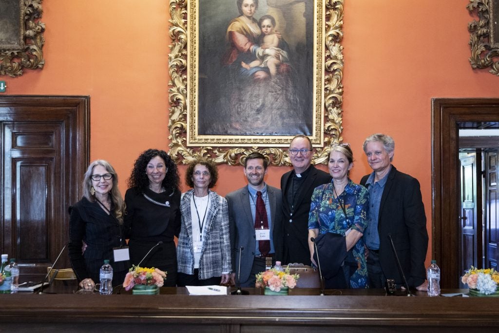 Four women and two men standing for a photo under a painting.