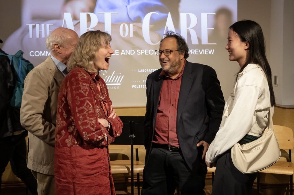 A group of four people smile at each other. Behind them is a screen that says "The Art of Care."