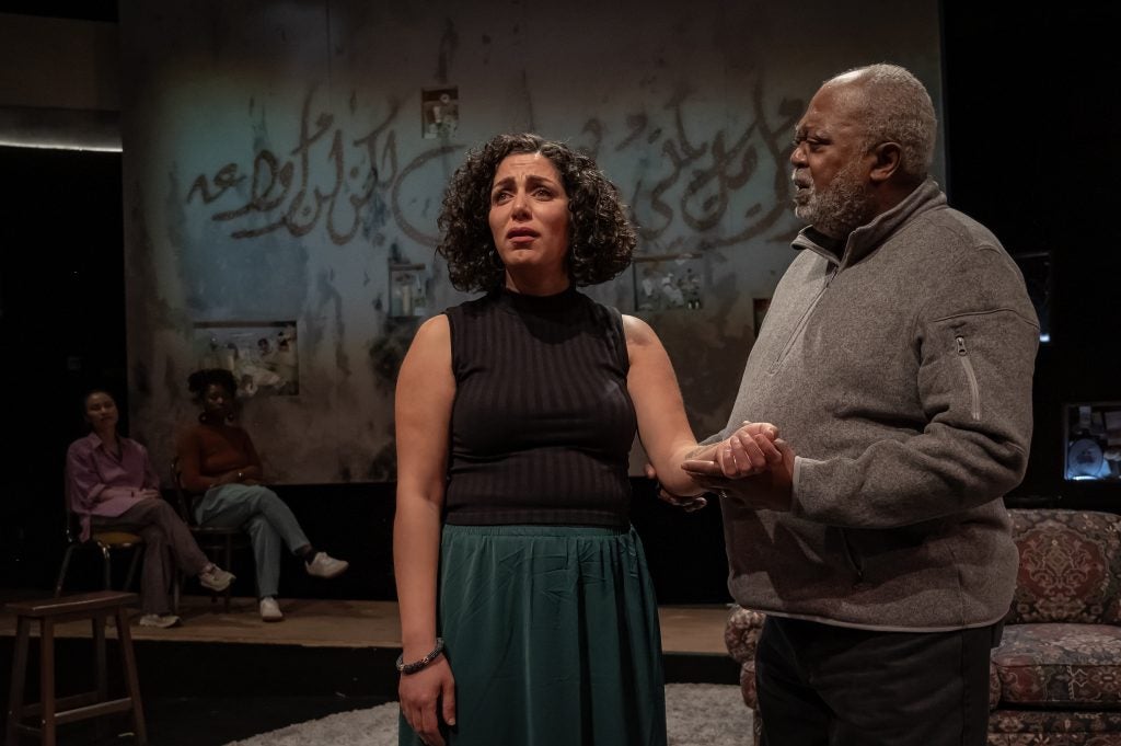 A man holds a woman's hand on a stage as they perform a play.