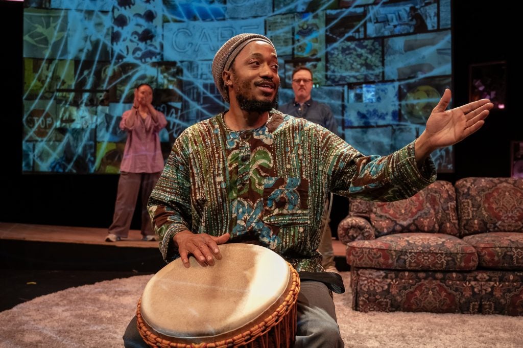 A man with a colorful green shirt plays a drum on a stage.