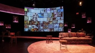 A stage is set with a couch on a carpet in front of a screen filled with mosaic images.