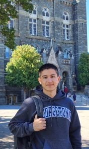 A male student with a Georgetown sweatshirt and a backpack stands on campus at Georgetown.