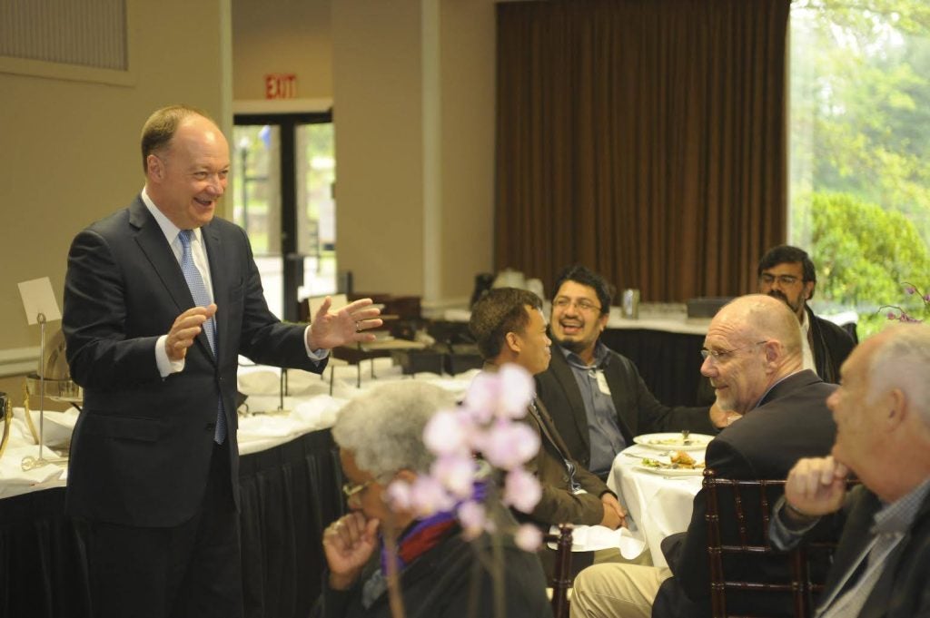 President DeGioia gestures to a group of attendees who are seated at round tables.