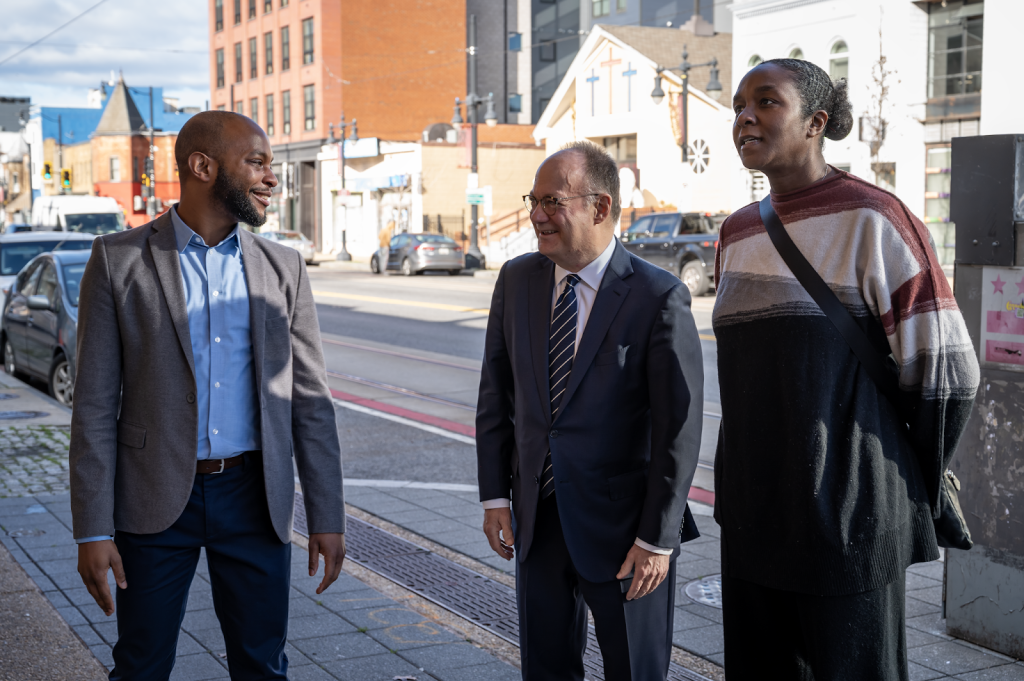 Two men and a woman speak and smile on a street in downtown Washington, DC.