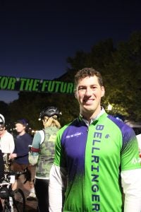 A man in a green bike jersey smiles in front of a banner at night.