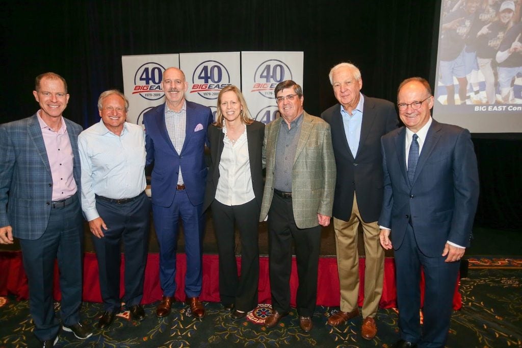 A group of men and a woman pose in front of a sign that says "40th"