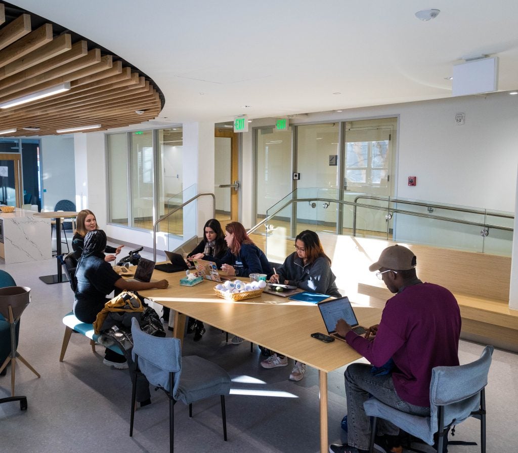 A group of Georgetown students sit at a rectangular table talking, working and studying.