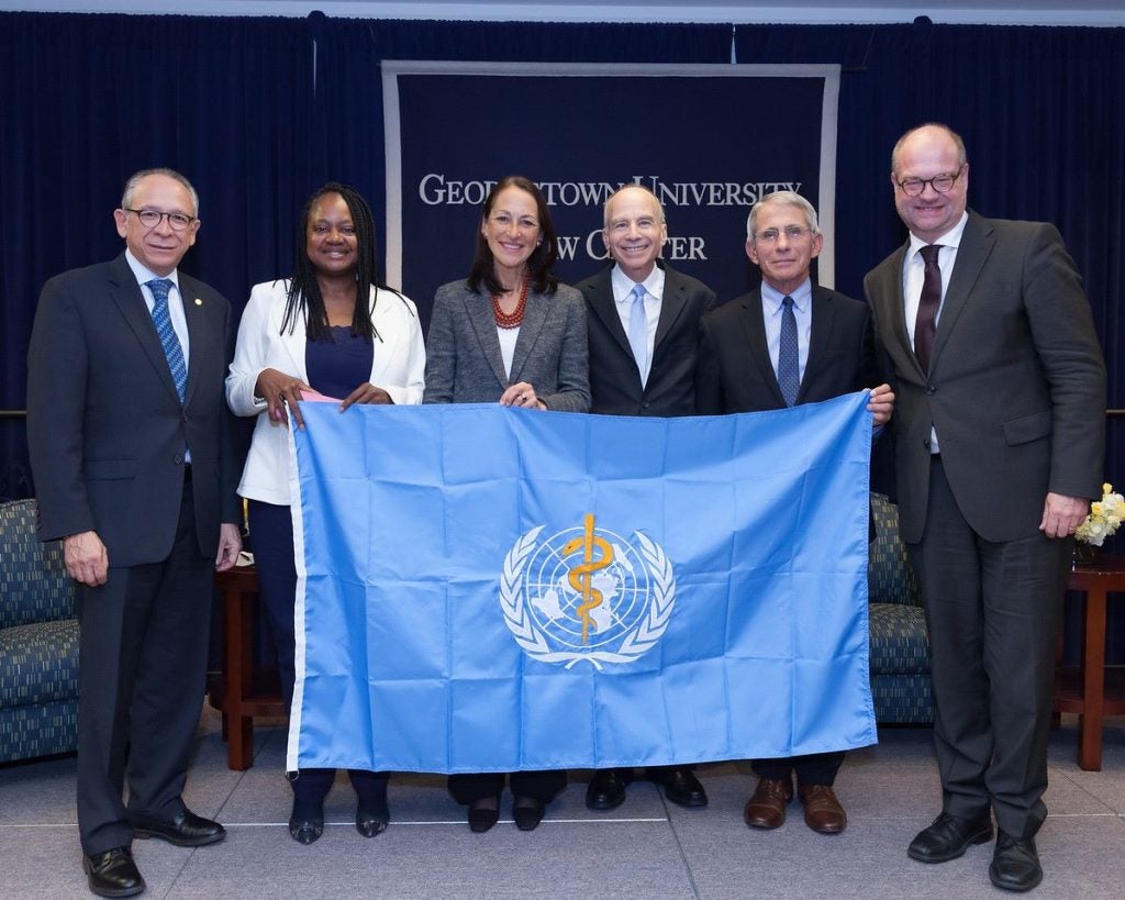 A group of men and women hold a blue flag in front of a sign that says "Georgetown University Law Center."