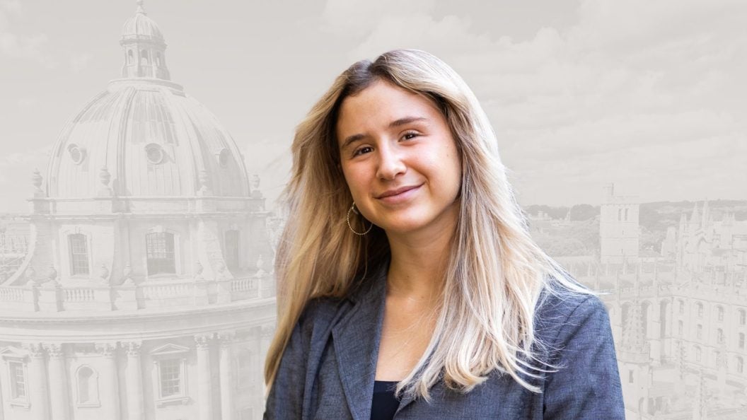 Noa Offman, a senior at Georgetown, smiles in front of a graphic of a building on Oxford&#039;s campus.