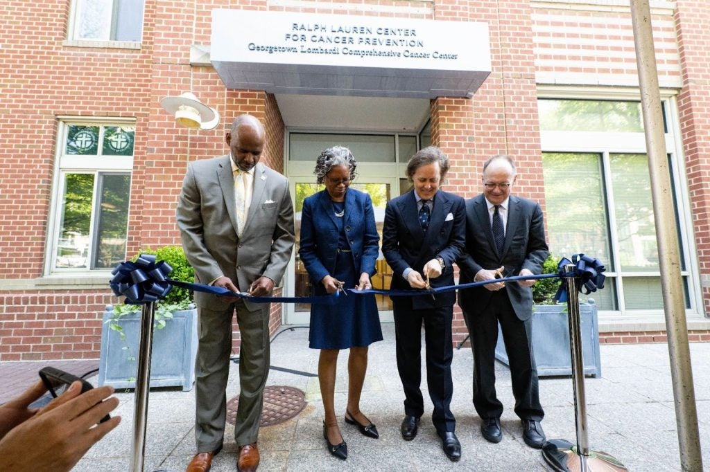 Four people cut a ribbon in front of a new building.