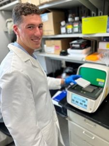 A student in a white coat works in a lab.