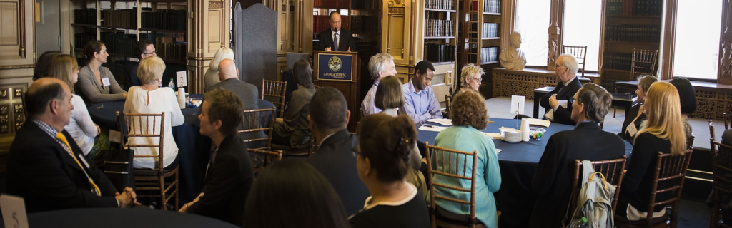 President DeGioia speaks in a library to a group of men and women seated at round tables.