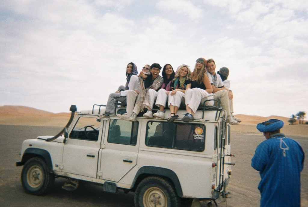 Students sitting on top of a white truck in a desert