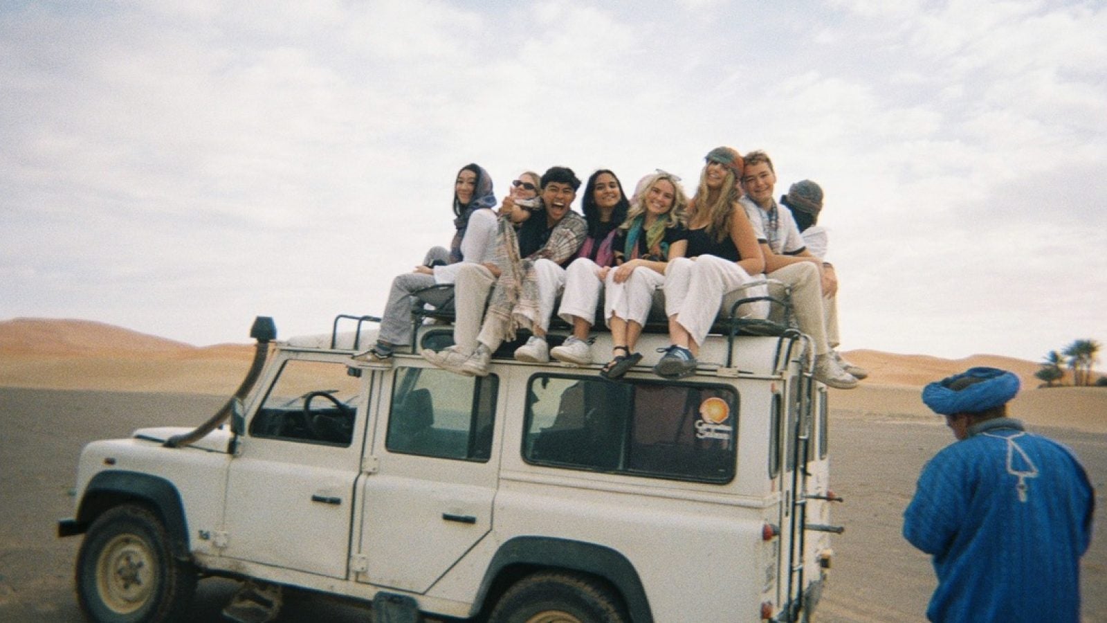 Students sitting on top of a white truck in a desert