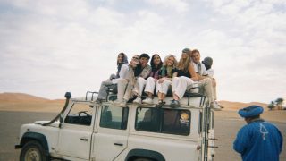 Students sitting on top of a white truck in a desert