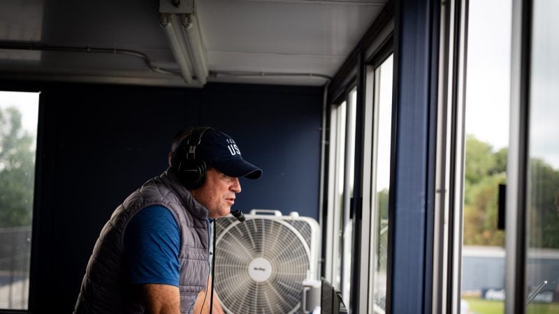 Dan Helfrich stands in the announcer&#039;s box while calling a men&#039;s soccer game.