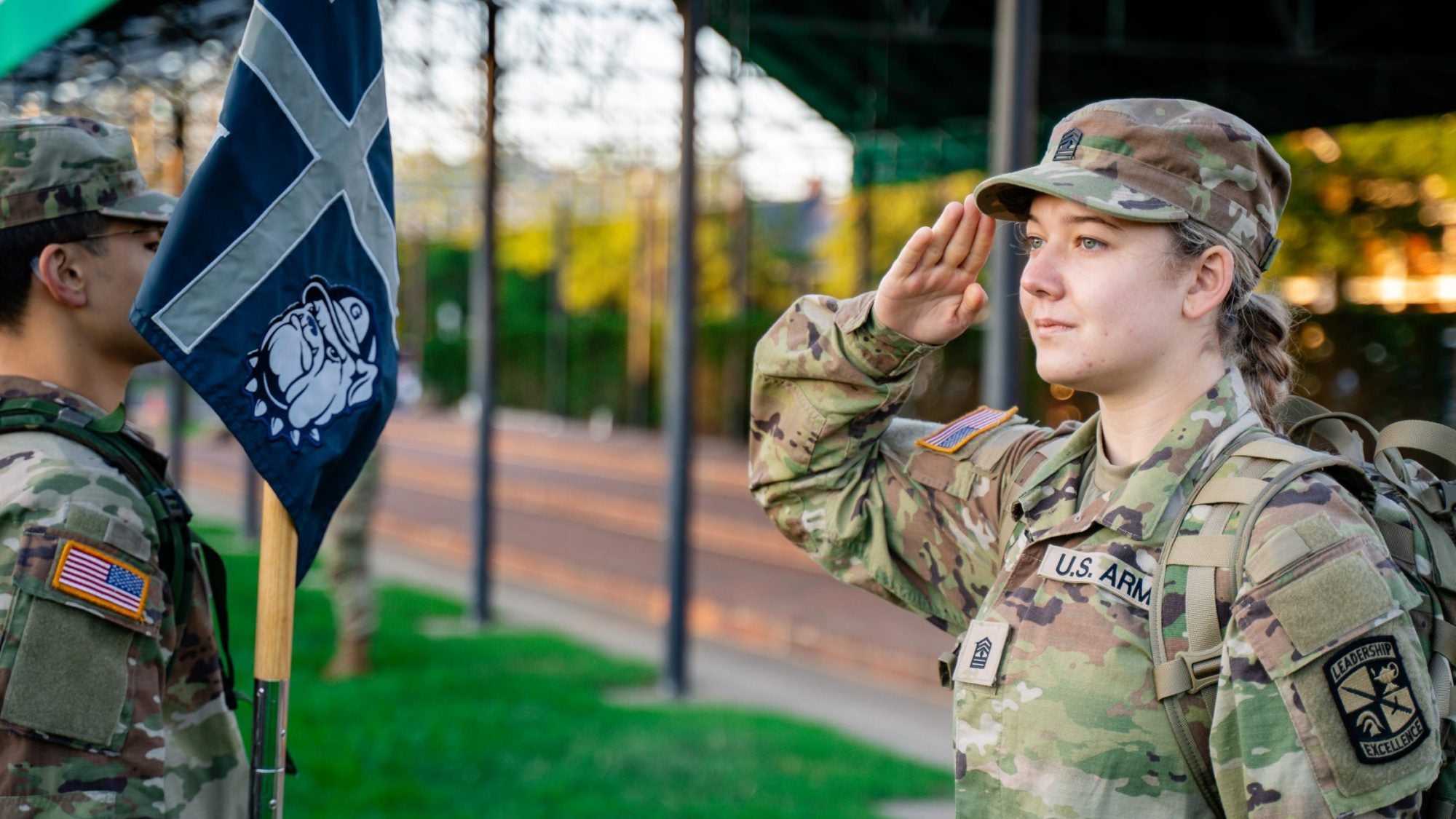 A young Army cadet in her uniform saluting another soldier