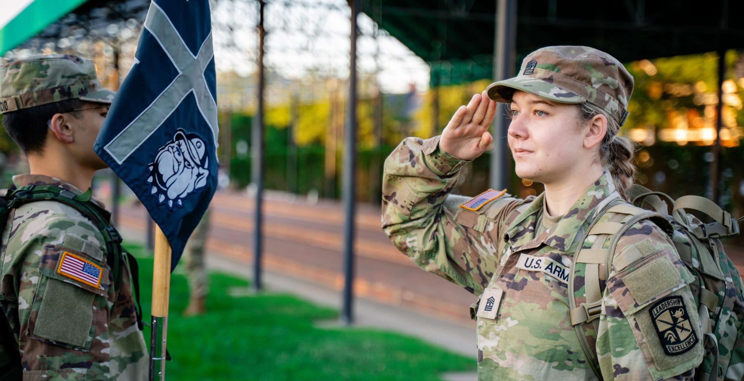 A young Army cadet in her uniform saluting another soldier