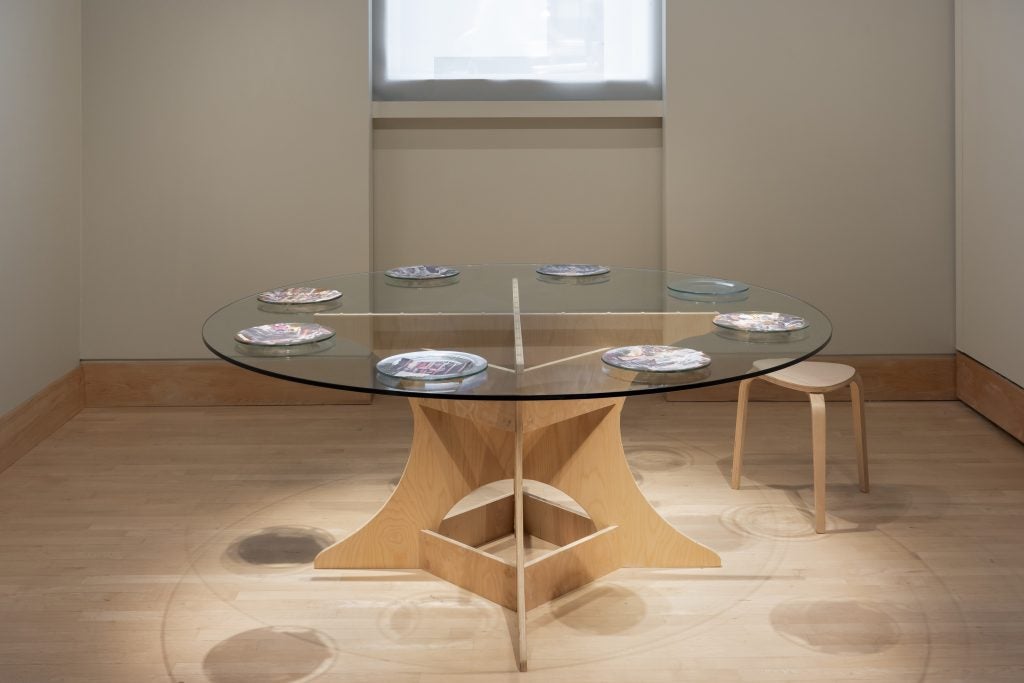 A glass round table set with eight plates as part of an exhibit at an art gallery.