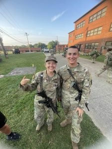 Two Army cadets pose for a photo strapped with assault rifles