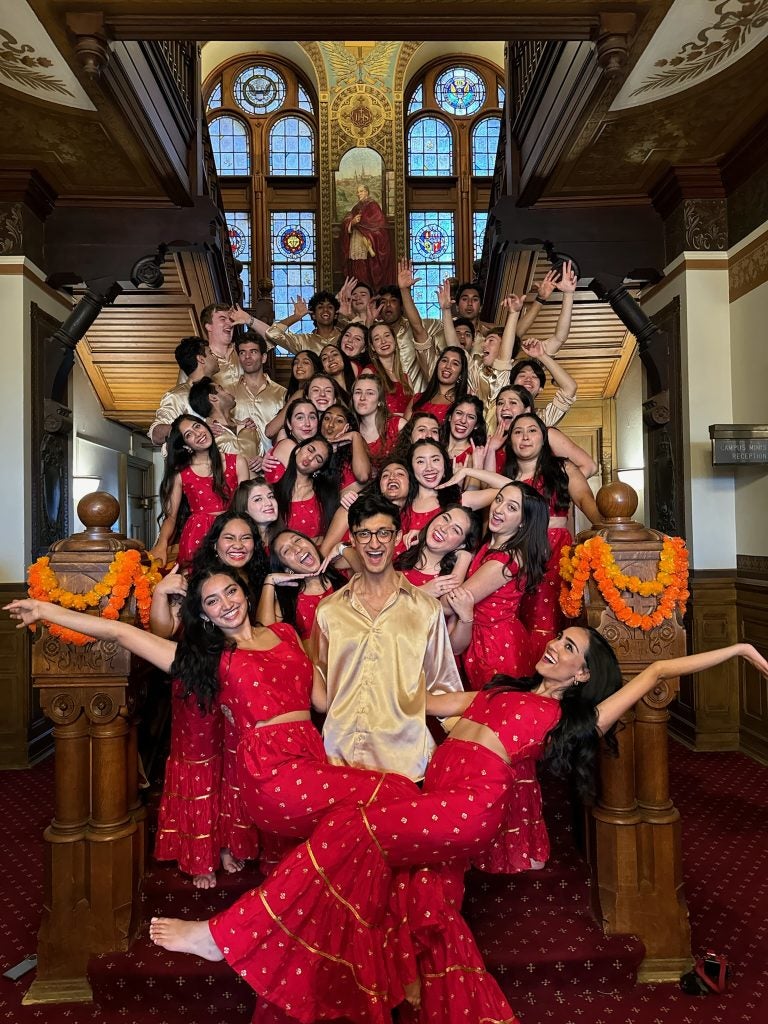 A group of dancers in red performance attire pose for a photo at a staircase