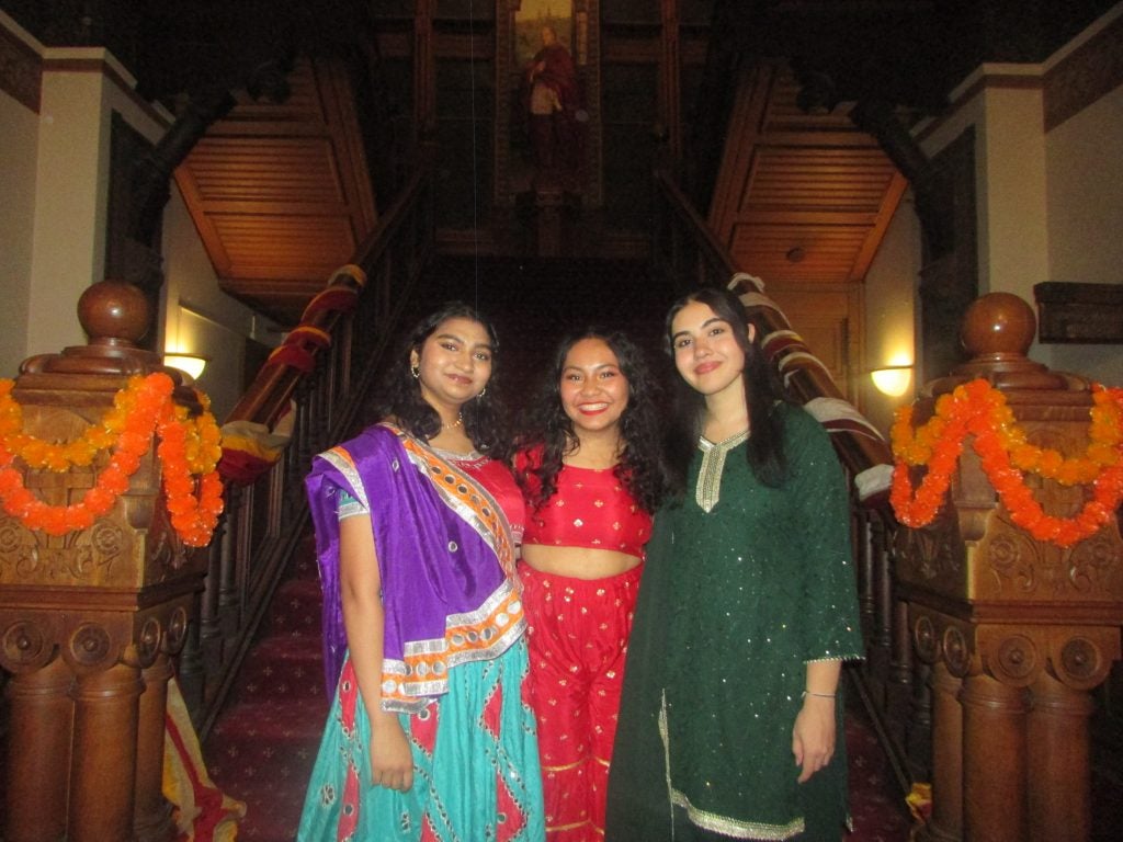 Three young women in South Asian attire in front of a staircase