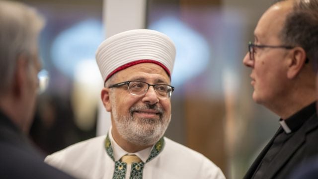 Imam Yahya Hendi smiles in a white robe and a traditional hat.