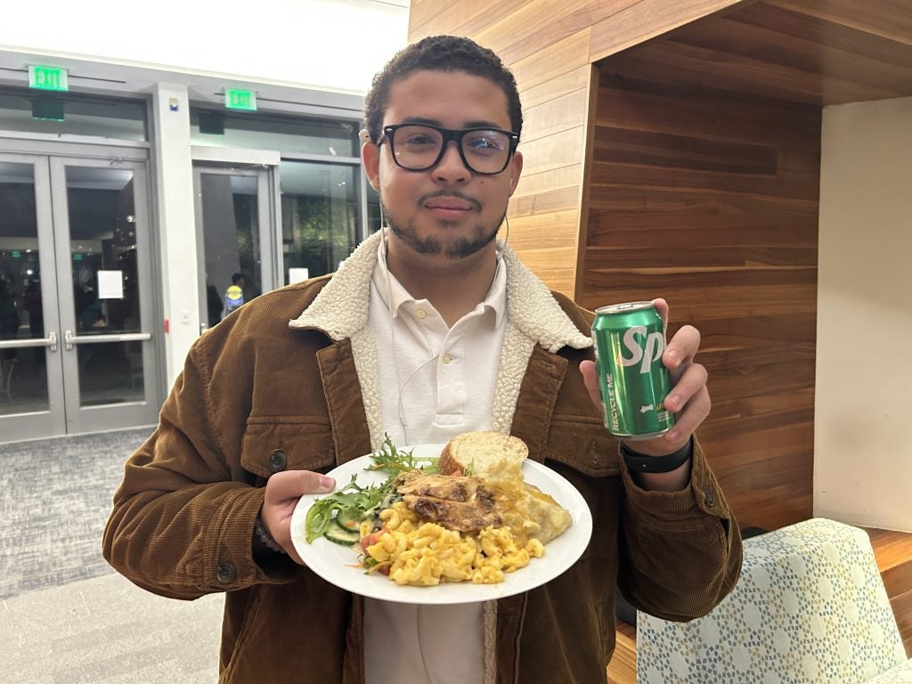 A young man holding a soda and a plate of food