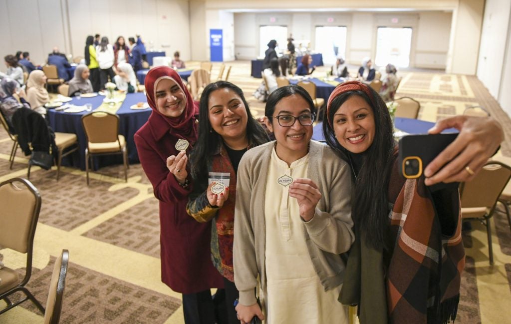 Four attendees of the 25th anniversary of Muslim Life take a selfie in a reception room.