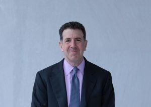 White male in a dark blue suit and pink shirt and blue tie