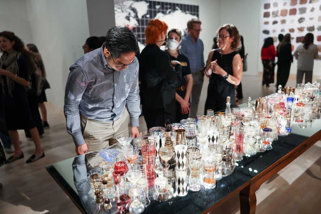 A man looks at a table covered in colorful antique glasses at an art gallery.