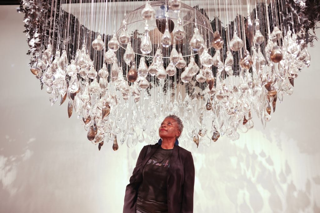 A woman stands underneath dangling hand-blown glass at an art gallery.