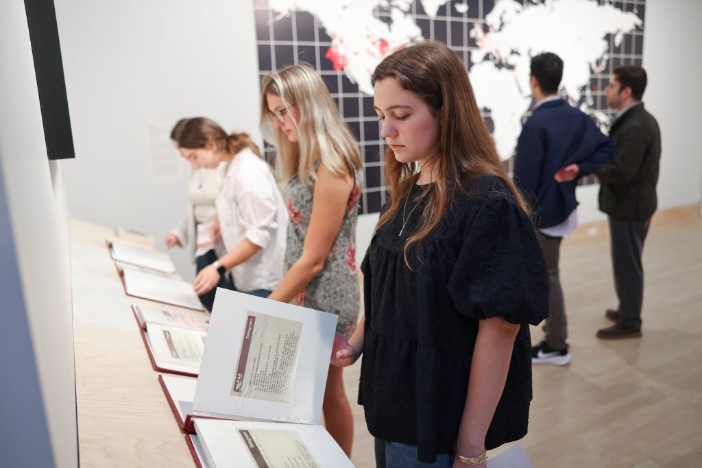 A young woman pages through a book of telegrams at an art gallery. Behind her is a world map.