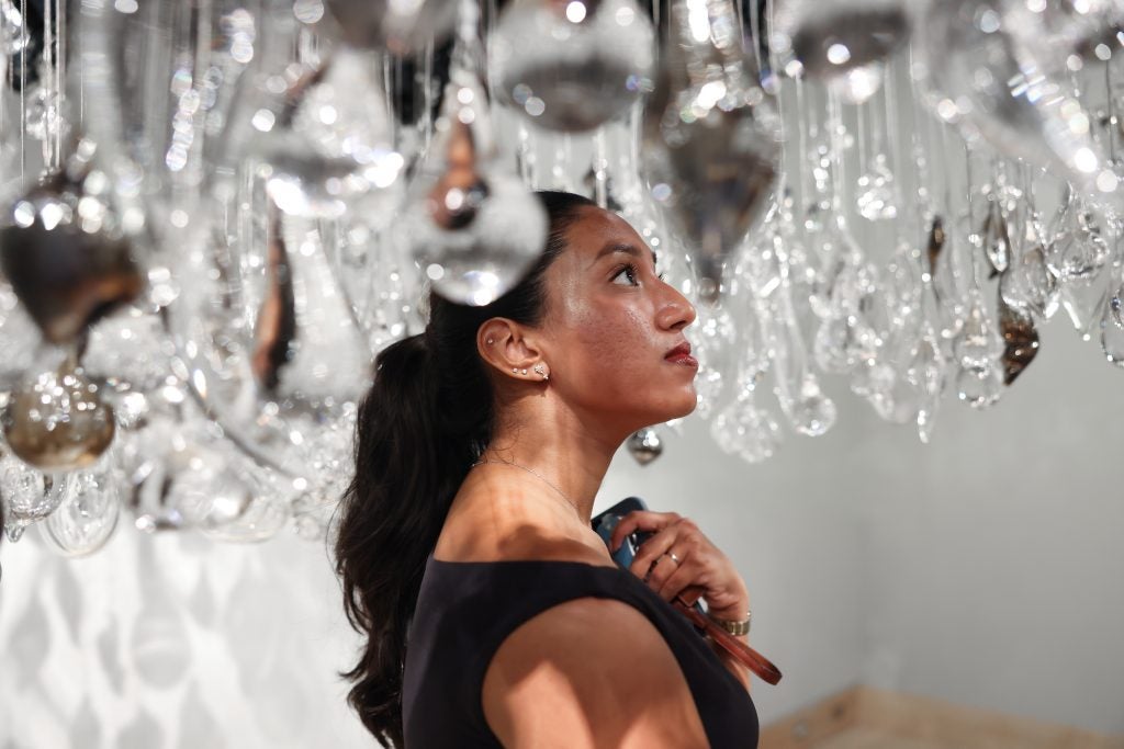 A woman stands underneath dangling hand-blown glass at an art gallery.