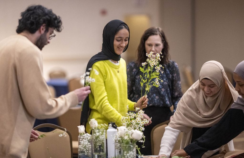 Two women and a male arrange flowers on a table. Two of the female students wear hijabs.