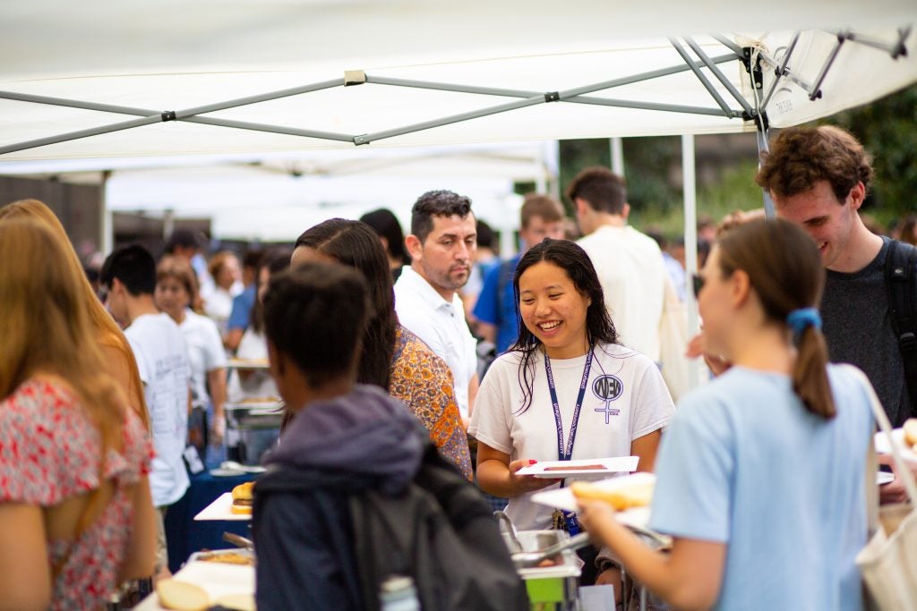 A student smiles in line at an outdoor buffet on Georgetown's campus.