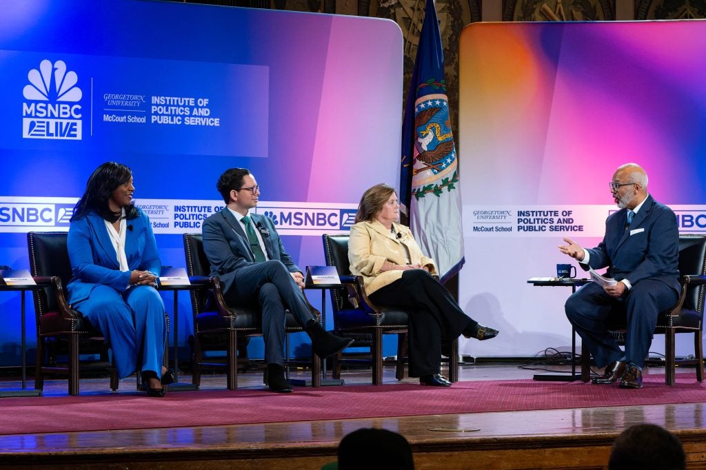 A man moderates a conversation with three people on stage