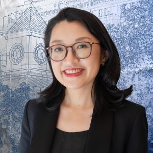 A woman with glasses, black hair, and a black blazer smiles in front of a blue textured graphic of a clocktower.