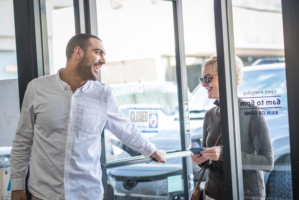 A man holds open a door for a woman at a coffee shop.