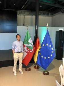 Shaun Ho stands next to three flags inside a room