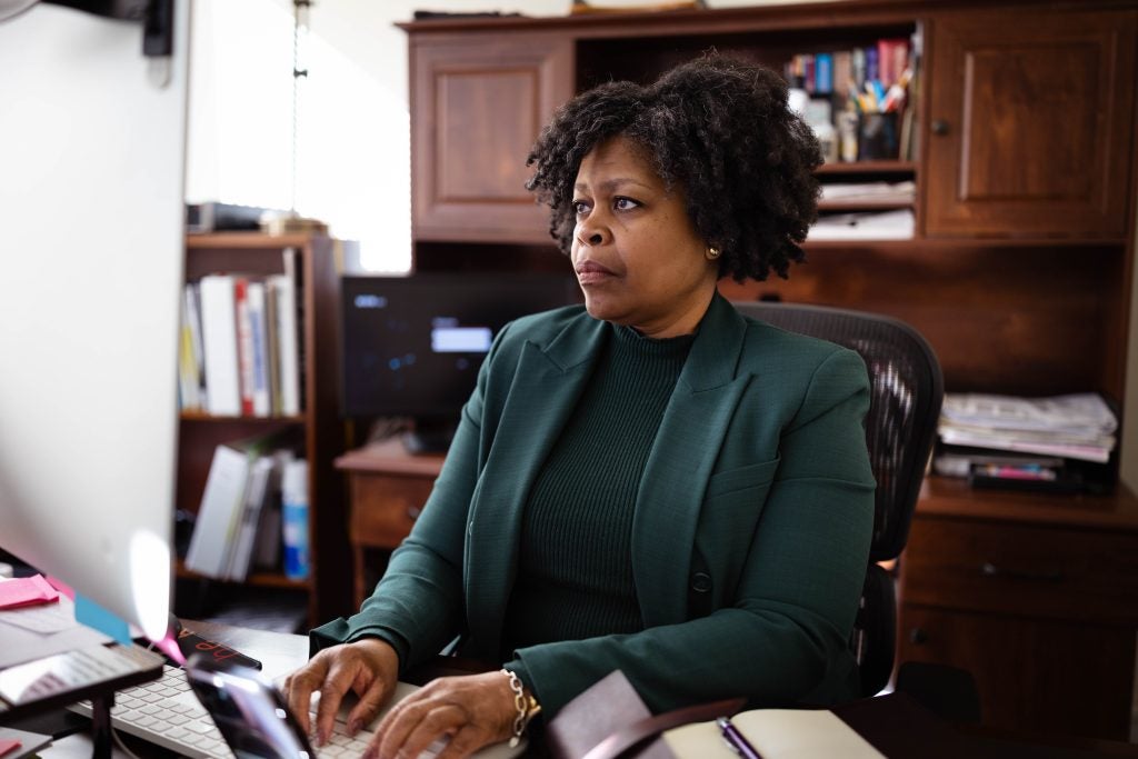 A woman looks at a computer screen with her hands on the keyboard. She wears an emerald green shirt and blazer.