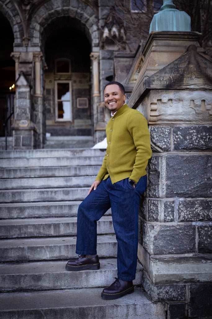 A man in a green sweater stands on stone steps outside Georgetown.