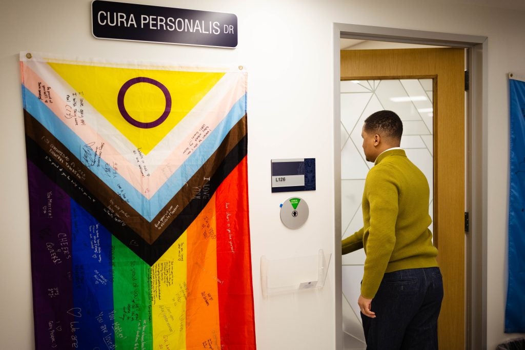 Lionell Daggs enters his office with a LGBTQ flag to his left on the wall